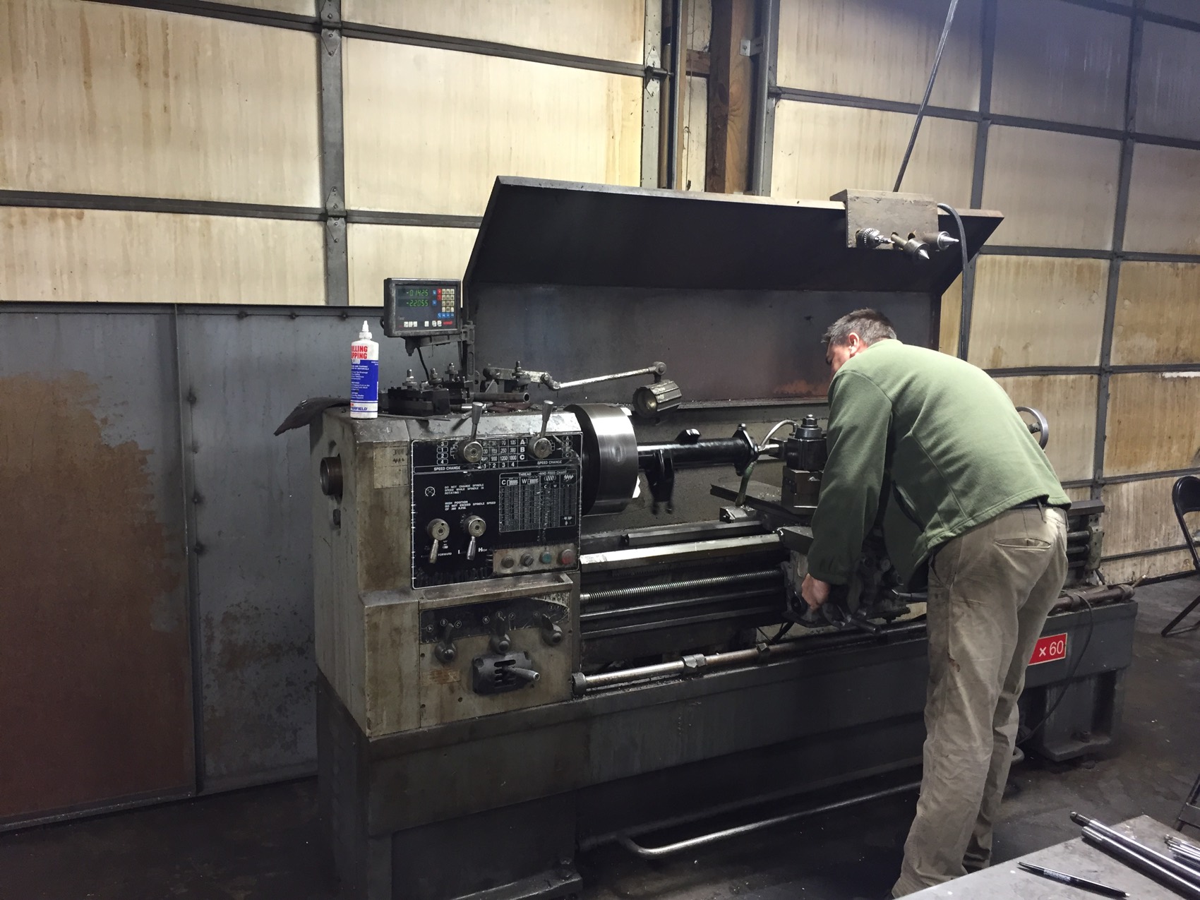 A machinist turning a part on a manual engine lathe with digital readout